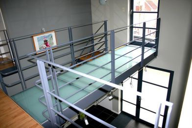 Passerelle d‘escalier avec garde-corps en lisses et sol en verre.